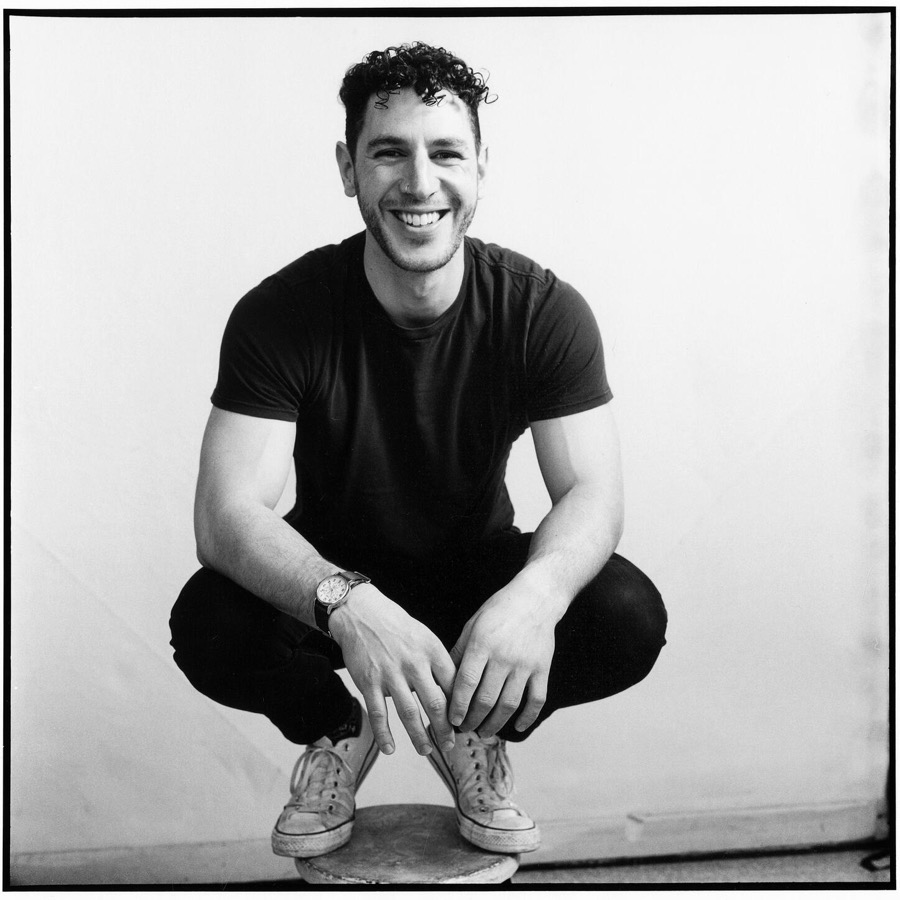 Adam Dexter, artist, director and startup founder coach, San Francisco — black-and-white portrait crouching on a stool, smiling